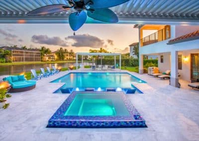 A modern pool and flush spa with a large covered patio and pergola at a waterfront Lighthouse Point home at sunset.