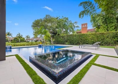 A modern, flush-mount spa with iridescent mosaic tile, set in a paver and turf deck at a home in Palm Beach Gardens.