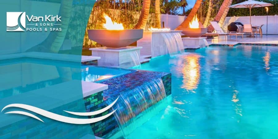 A modern pool at night in Davie with a lighted waterfall wall and two large fire and water bowls.