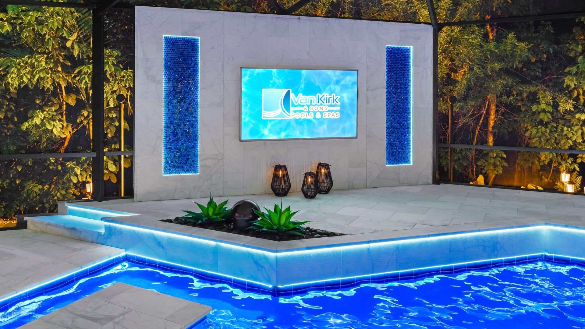A custom outdoor TV wall with backlit blue mosaic tile and integrated LED lighting along the deck of a modern pool.