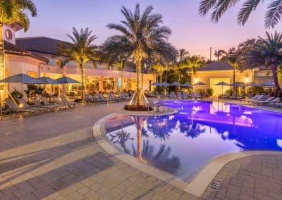 The large, freeform resort pool at Addison Reserve in Delray Beach, built by Van Kirk Pools, glows with purple LED lights at twilight.