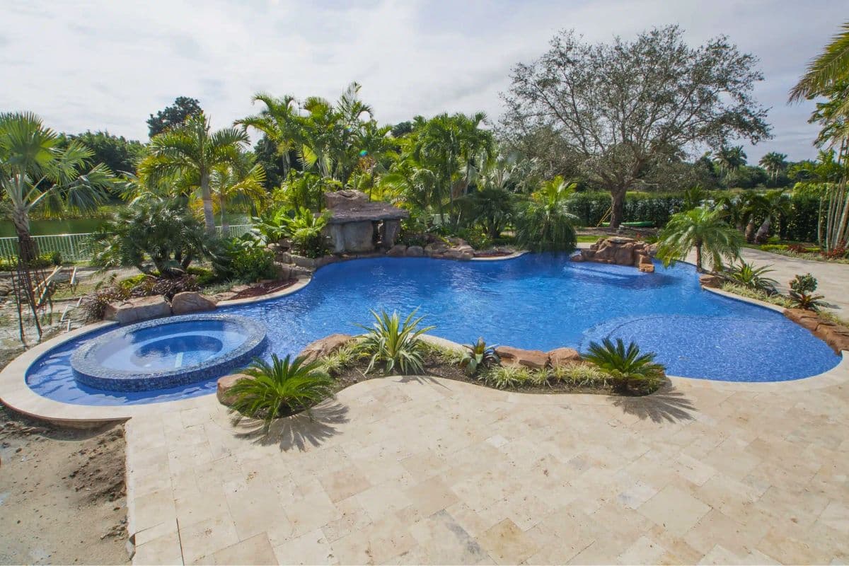 A large, newly built tropical freeform pool with a rock grotto and a round spa in a Southwest Ranches backyard.