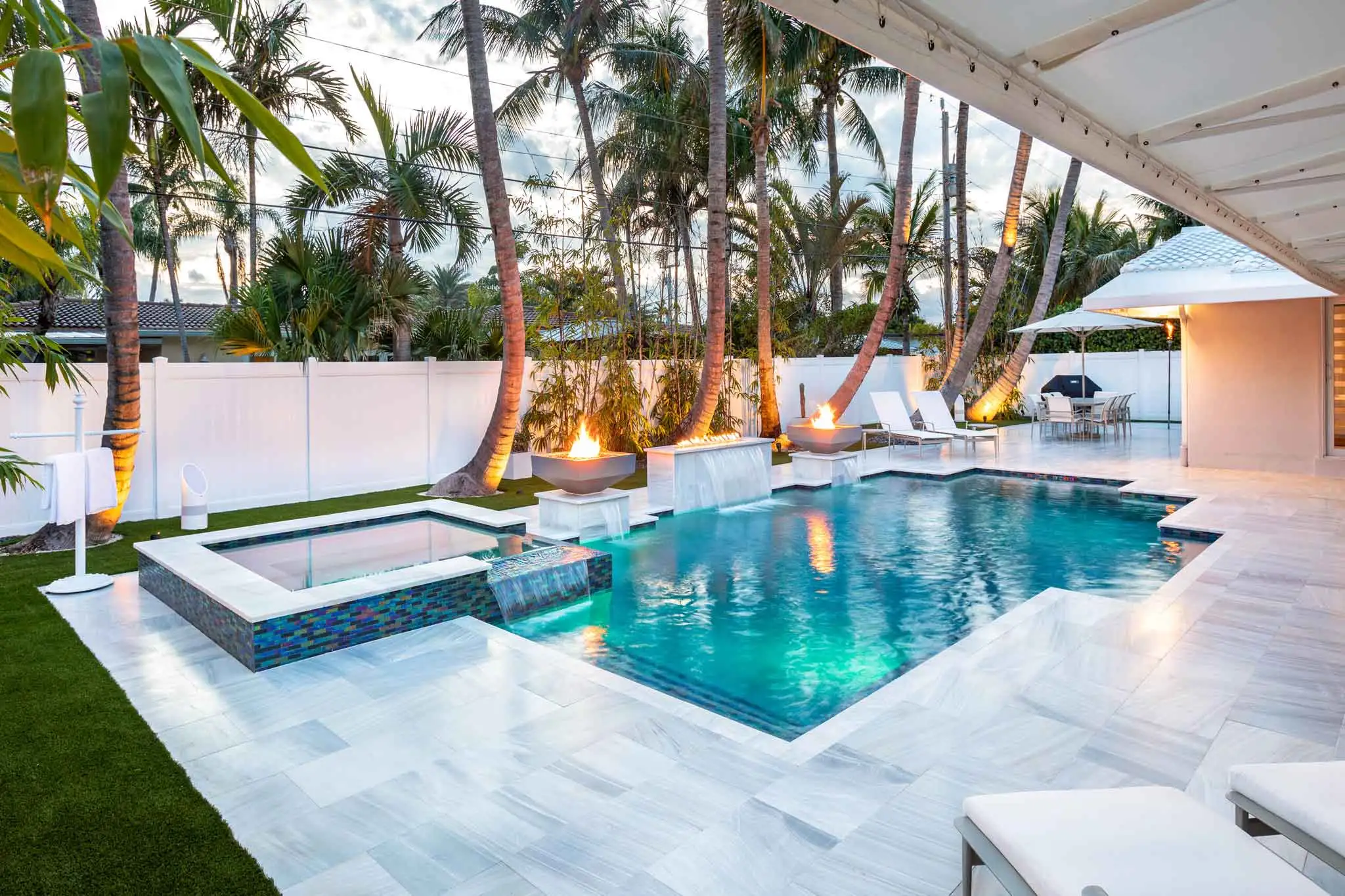 Modern tropical backyard with luxury pool, spa, and fire features surrounded by palm trees and elegant marble decking.