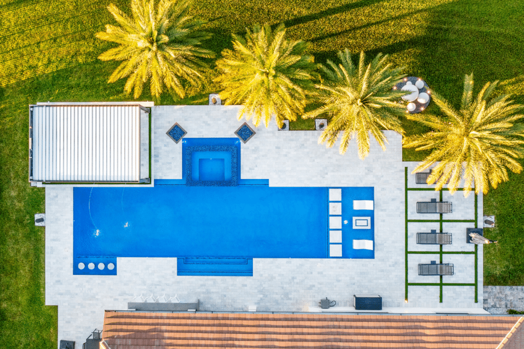 Aerial view of a custom lap pool with bubblers, sun shelf, and surrounding palm trees.