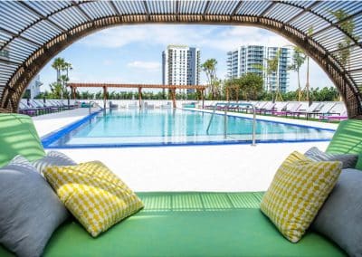 View of the rectangular commercial pool through a woven cabana arch on the Downtown Fort Lauderdale apartment high-rise amenity deck, by Van Kirk & Sons.