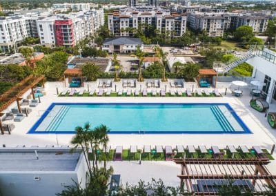 High aerial view of a large rectangular commercial pool on a high-rise rooftop amenity deck in Downtown Fort Lauderdale, with surrounding landscaping.