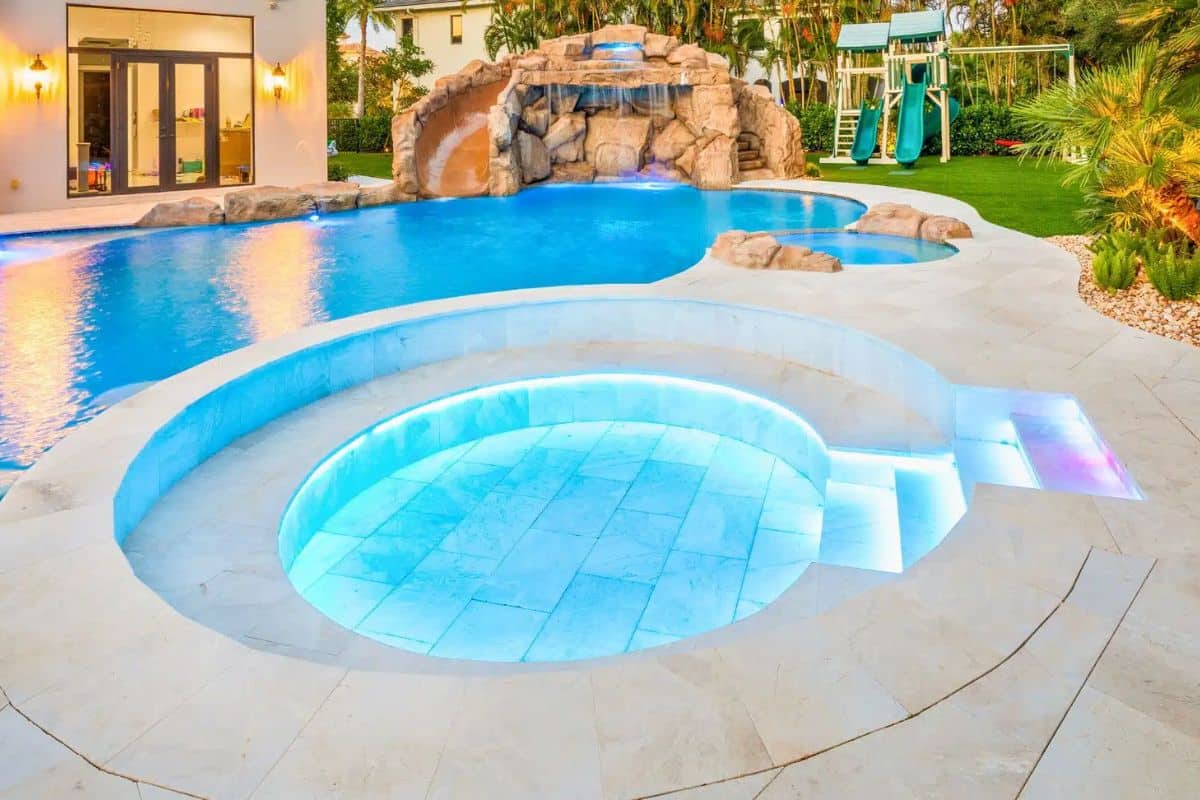 Freeform backyard pool with natural rock waterfall, curved water slide, integrated spa, steps, and professional LED lighting system