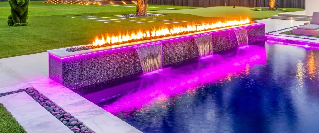 Modern pool with fire and water features illuminated by purple LED lighting at night in Boca Raton