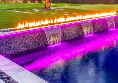 Modern pool with fire and water features illuminated by purple LED lighting at night in Boca Raton