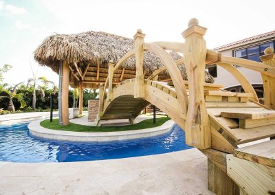A custom wooden bridge leads to a tiki hut island over a lazy river, built by Van Kirk Pools for "The Vanilla Ice Project."