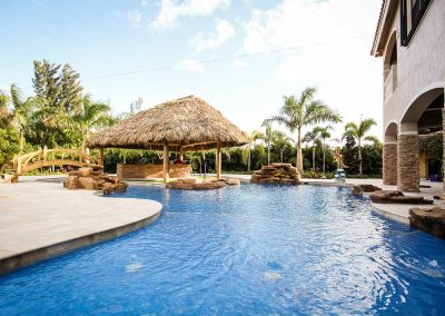 The "Vanilla Ice Project" lagoon pool by Van Kirk Pools, featuring a large tiki hut bar, rock spa, and lazy river in a tropical South Florida backyard.