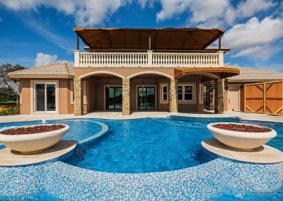 The "Vanilla Ice Project" pool by Van Kirk Pools, featuring two large fire bowls, a raised spa, and a custom blue mosaic tile waterfall.