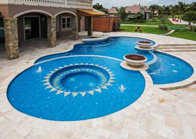 A wide view of the "Vanilla Ice Project" pool by Van Kirk, featuring the custom sun mosaic spa, two fire bowls, and a travertine patio.