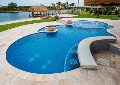 A reverse view of the "Vanilla Ice Project" pool by Van Kirk, showing the swim-up bar, in-pool stools, sun mosaic spa, and a waterfront tiki hut.