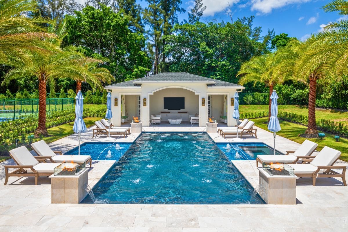 Van Kirk Pools built this modern South Florida pool with unique waterfall loungers, a raised spa, and a white pergola.