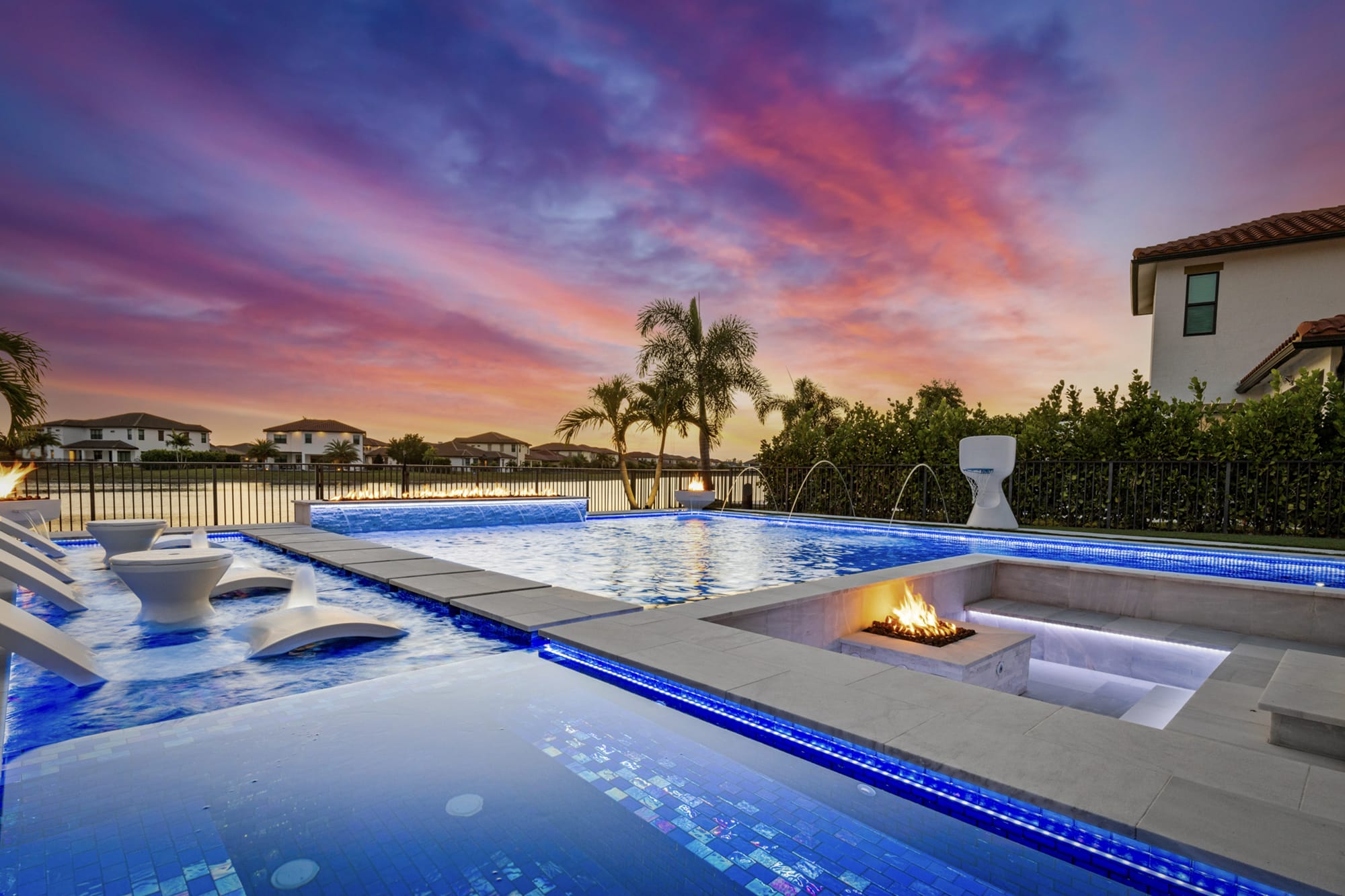 Rock waterfall flowing into a backyard swimming pool with a stone patio and lush greenery in the background of a lake worth home.