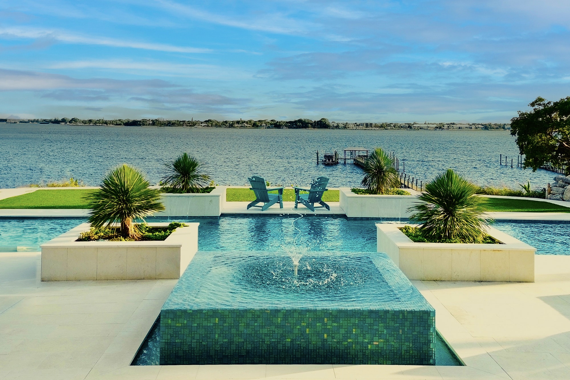 Luxury pool and modern home exterior at night with colorful lighting, palm trees, and a wet edge swimming pool.