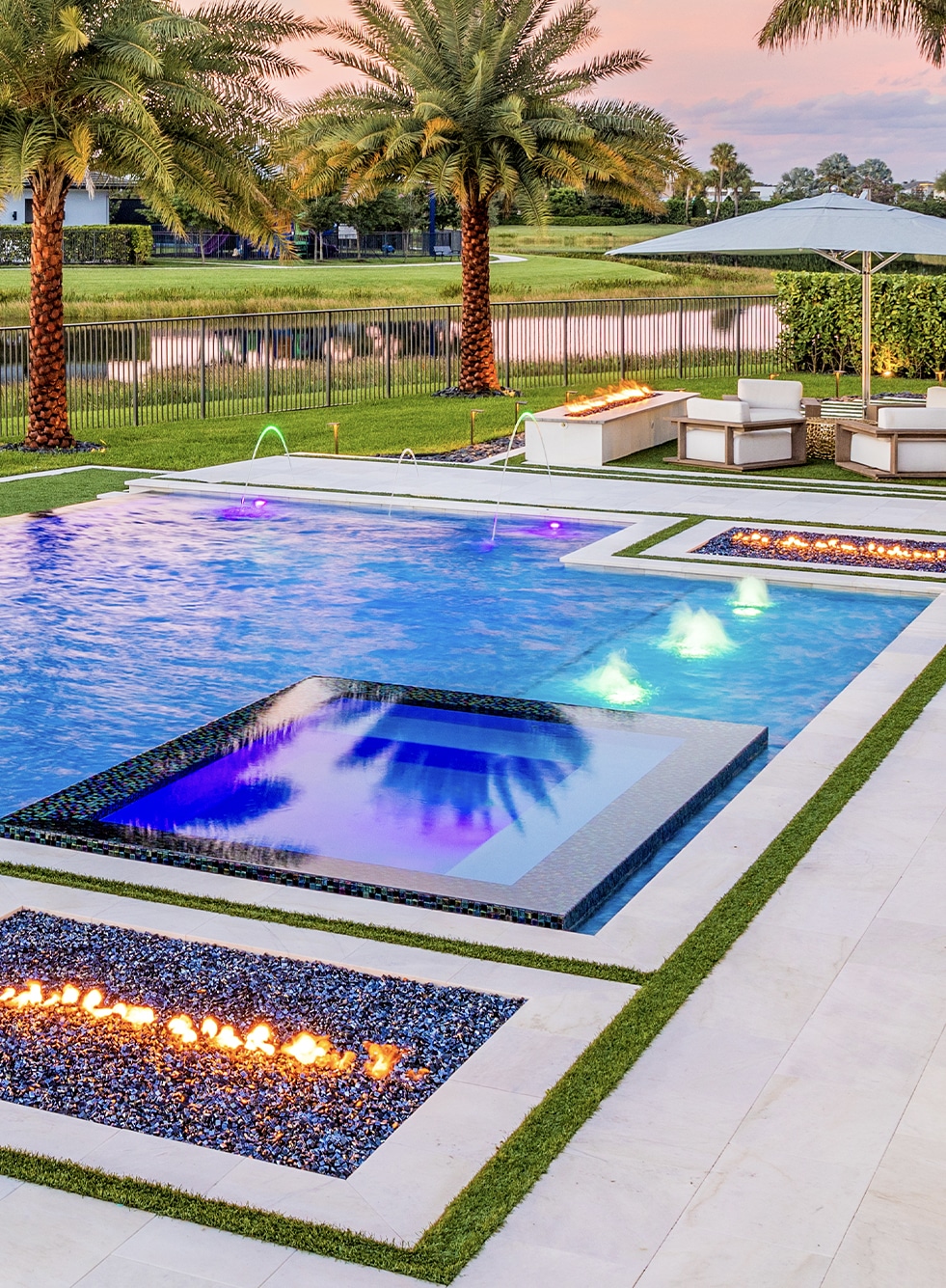 Luxury backyard with a modern pool, lounge chairs, and vibrant lighting at sunset.