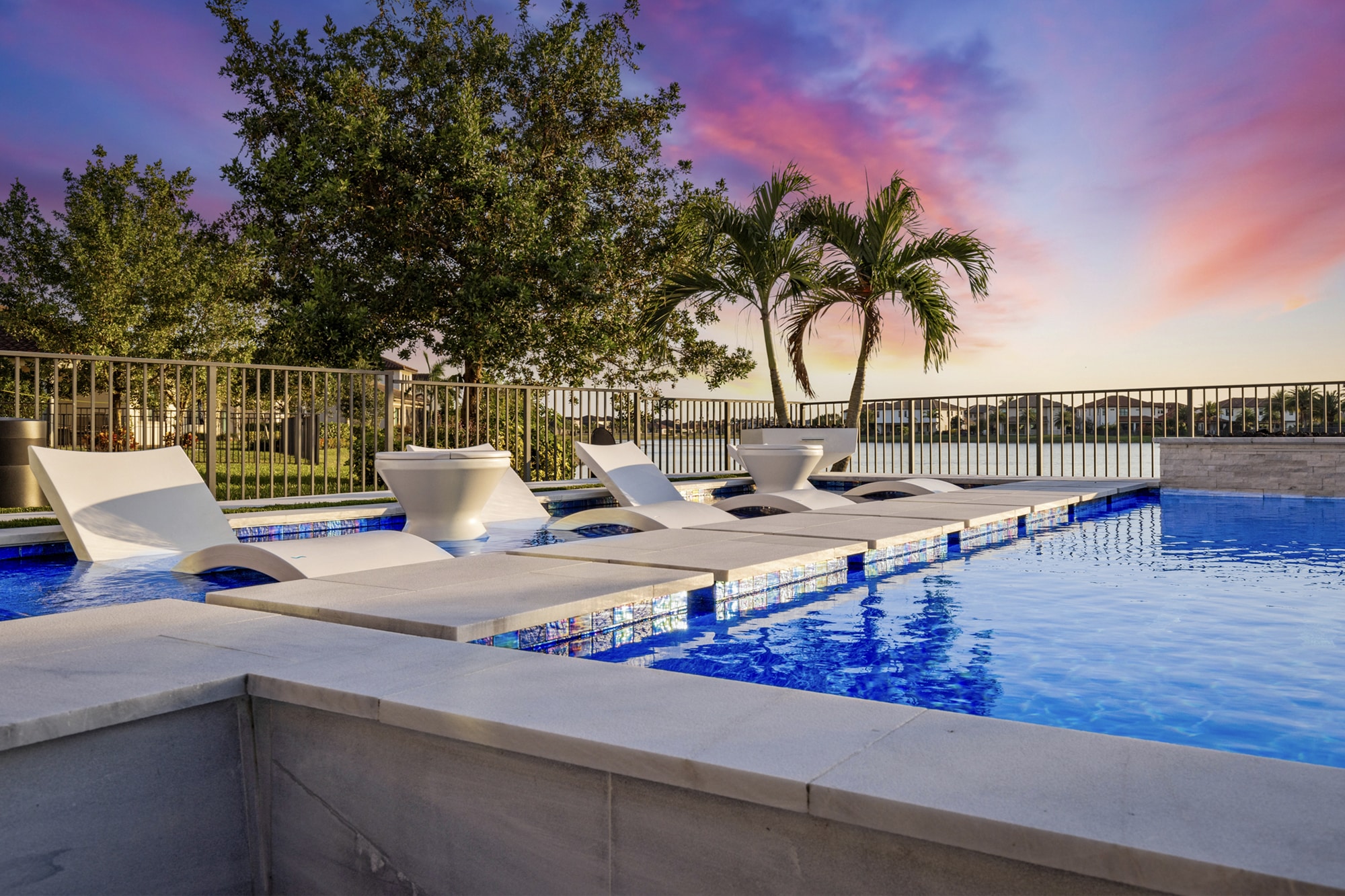Luxury waterfront mansion featuring a modern infinity pool, palm landscaping, and panoramic water views in a contemporary outdoor living design.