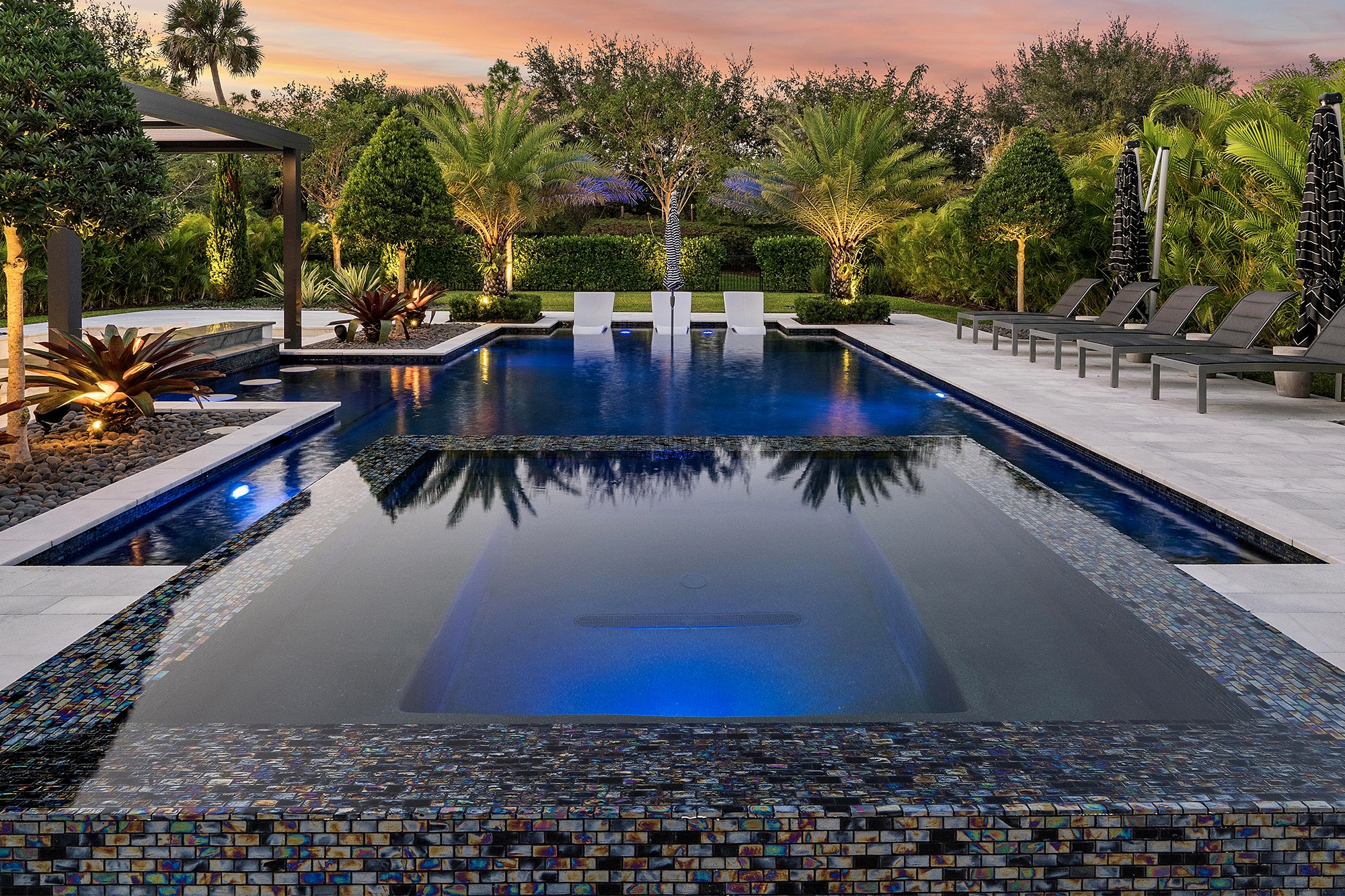 Luxurious outdoor pool designed by Fort Lauderdale pool contractor Van Kirk & Sons with modern seating area, palm trees, and pergola, perfect for relaxation and entertainment.