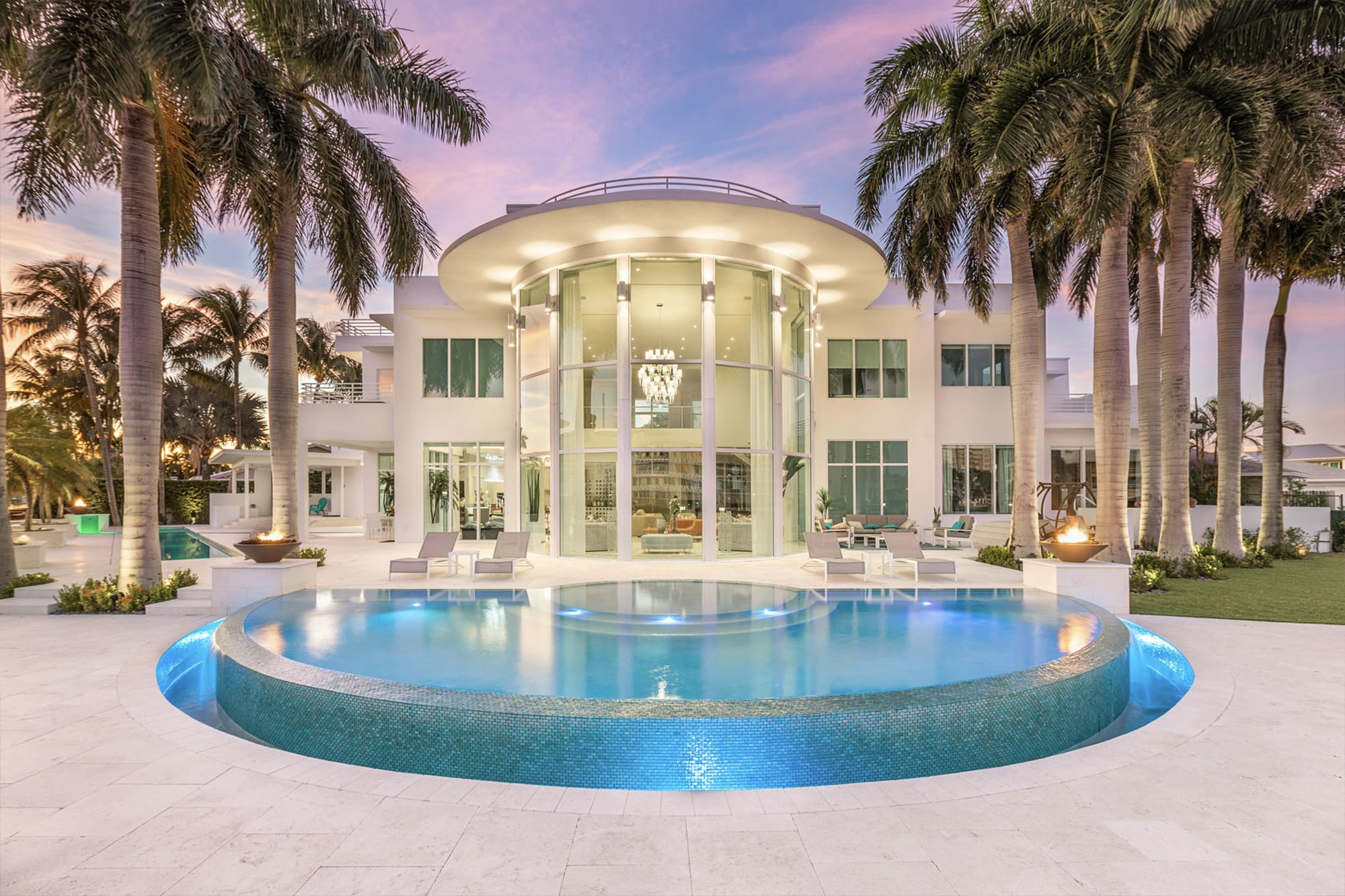Luxurious poolside view with palm trees, waterfront backdrop, and sunset sky at a modern villa.