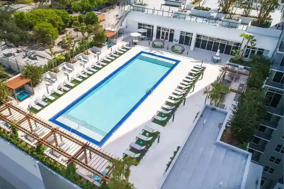 downtown-ftlaud-apartment-pool-urban-aerialjpg_11zon - Van Kirk & Sons Pools & Spas Rectangular rooftop swimming pool surrounded by lounge chairs and greenery on a sunny day afar